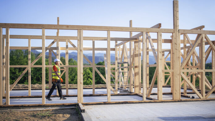 Builder Working On Wooden House In Nature. Housing starts new home construction